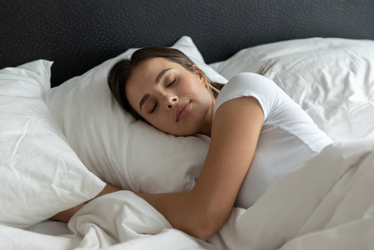 Relaxed young female sleeping in large cosy bed at home or in hotel suite room on clean white bedclothing hugging soft pillow covered with warm blanket dreaming resting having pleasure